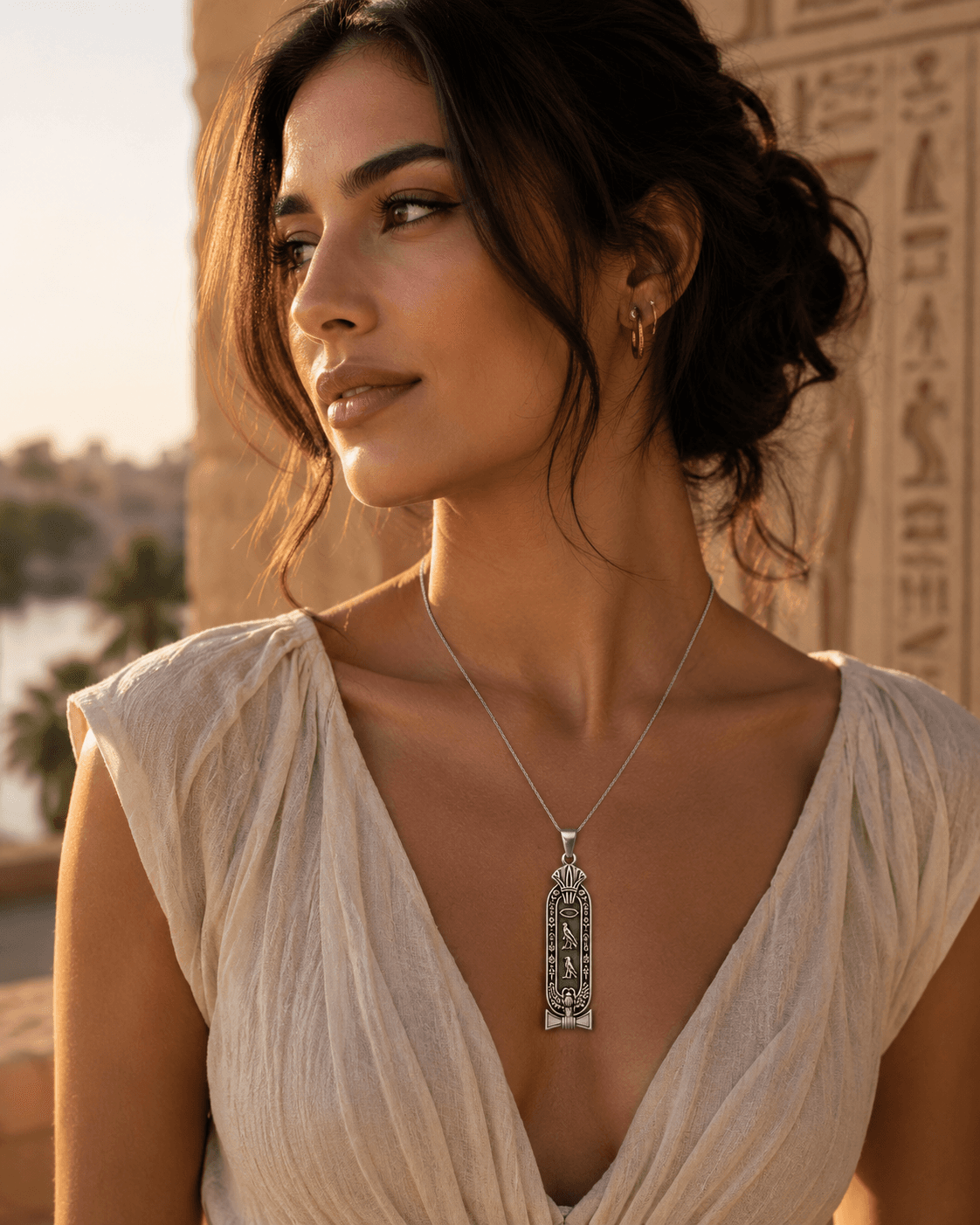 A woman wearing a gold hieroglyph cartouche pendant, photographed at an ancient Egyptian temple